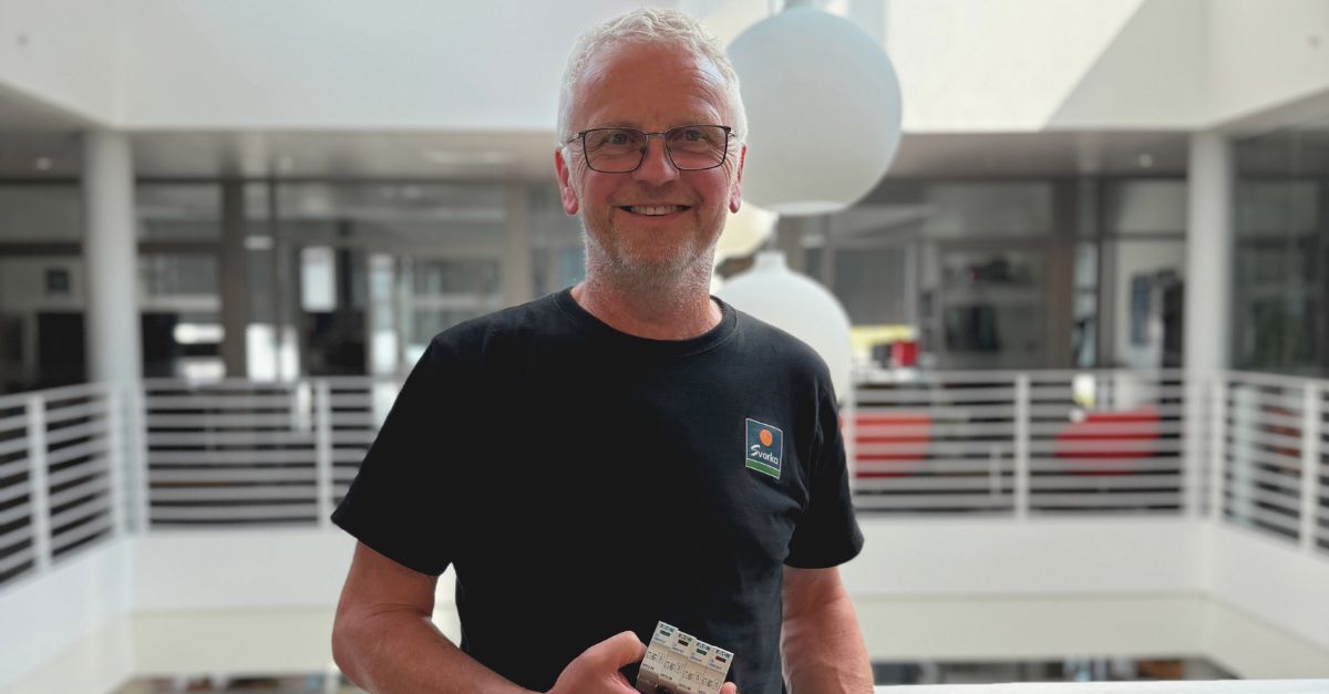 Mann ser mot kamerat og smiler, holder et overspenningsvern i hånda. 