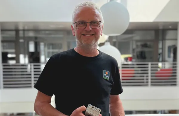 Slik sikrer du boligen din mot lynnedslag i ferien Mann ser mot kamerat og smiler, holder et overspenningsvern i hånda.