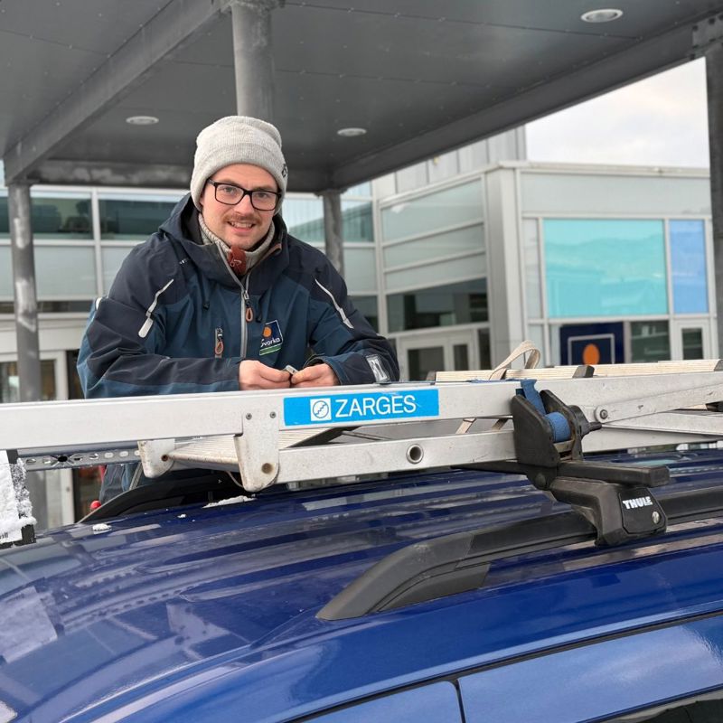 Bilde av en elektriker som fester en stige til taket på arbeidsbilen. Han ser i kameraet og smiler. 